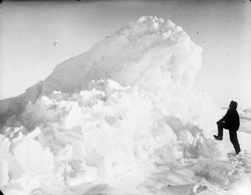 Fotografía en blanco y negro de Frank Worsley, pequeño junto a una enorme cresta de hielo en el mar de Weddell